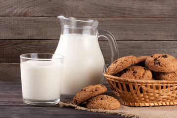 jug and glass of milk with oatmeal cookies in a wicker basket on a wooden background