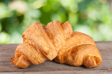 two croissant on a wooden board with a blurry garden background
