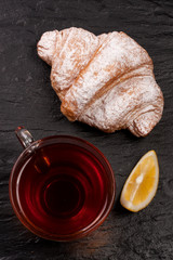 croissant with a cup of tea on a black stone background. Top view