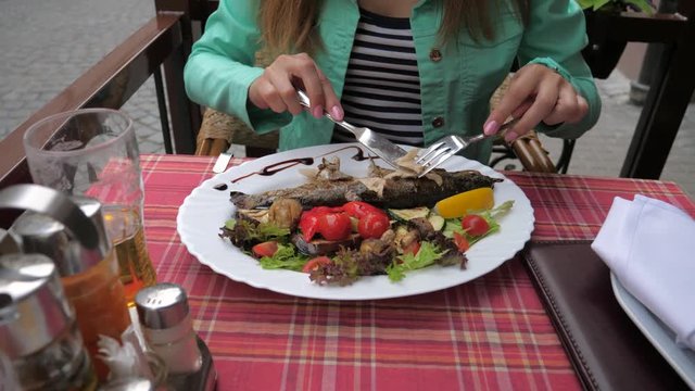 Eating baked fish with vegetables in restaurant closeup.