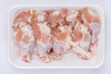 A white foam tray of raw chicken drumsticks from supermarket on white background, fresh food ingredients concept.