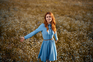 Beautiful young woman in a blue dress is standing in a field of flowers