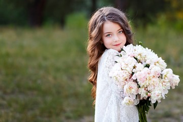 Naklejka premium little girl six years old with brown hair and blue eyes with a bouquet of peony flowers wearung white dress, smiling