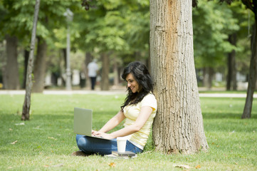 Attractive beautiful latin woman happy working on her laptop outside in a green park