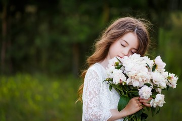 Naklejka premium little girl six years old with brown hair and blue eyes with a bouquet of peony flowers wearung white dress, smiling