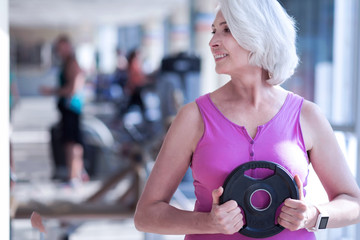Fototapeta na wymiar Aged woman holding barbell at gym