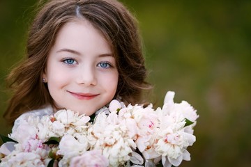 Fototapeta premium little girl six years old with brown hair and blue eyes with a bouquet of peony flowers wearung white dress, smiling