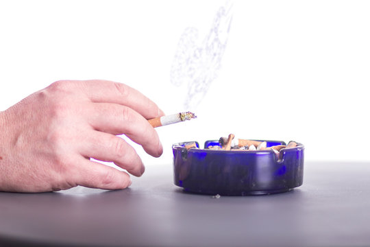 Hand hält eine Zigarette vor einem Aschenbecher 