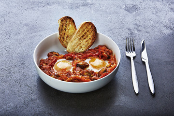 Shakshouka or shakshuka  a dish of eggs poached in a sauce of tomatoes, chili peppers, and onions, often spiced with cumin.