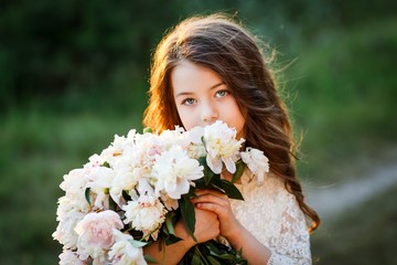 Fototapeta premium little girl six years old with brown hair and blue eyes with a bouquet of peony flowers wearung white dress, smiling