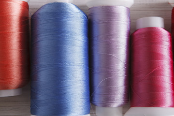 Colorful thread spools on wooden table close up