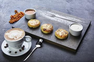 breakfast cheese pancakes with sea-buckthorn sauce and cappuccino on grey background