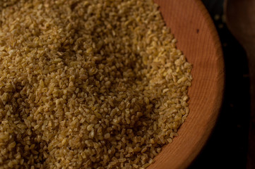 Dry bulgur wheat in brown wooden bowl isolated on dark wood