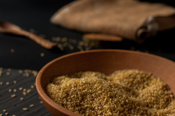 Dry bulgur wheat in brown wooden bowl isolated on dark wood