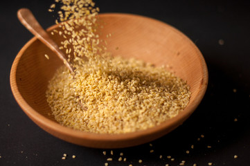 Dry bulgur wheat in brown wooden bowl isolated on dark wood