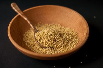 Dry bulgur wheat in brown wooden bowl isolated on dark wood