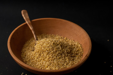 Dry bulgur wheat in brown wooden bowl isolated on dark wood