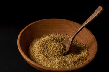 Dry bulgur wheat in brown wooden bowl isolated on dark wood