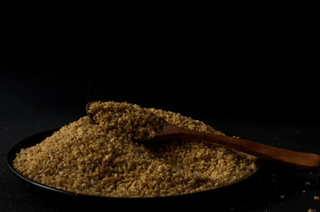 Dry bulgur wheat in brown wooden bowl isolated on dark wood