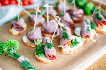 Delisious catering banquet buffet table decorated in rustic style in the garden. Different snacks, sandwiches with ham and pesto sauce. Outdoor, closeup.