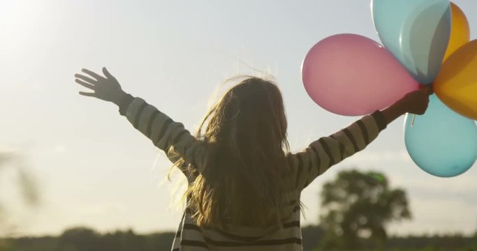 Dancing Little Girl with Colored Air Balloons in the Field Backlight