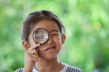 Asian little child girl looking through a magnifying glass on green nature background