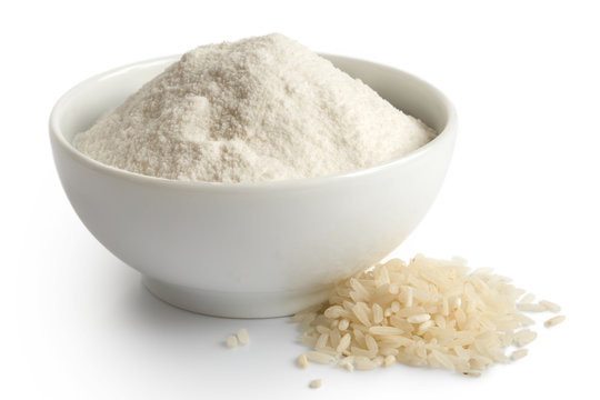White rice flour in white ceramic bowl isolated on white. Spilled rice.