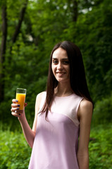 Beautiful slim girl drinks juice from a glass beaker in the park