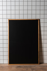 empty chalkboard in wooden frame standing at white tiled wall