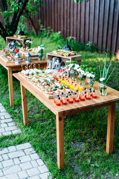 Beautiful catering banquet buffet table decorated in rustic style in the garden. Different snacks, sandwiches and cocktails. Outdoor, two tables with food under the tree. Vertical photo.