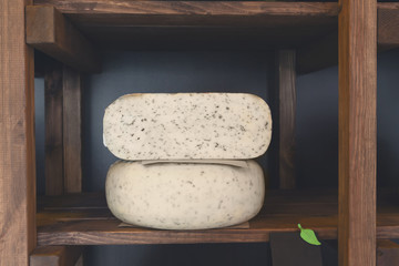 Hard cheese with herbs in wheel and piece on grocery shop shelf