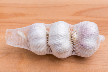 Packaged white garlic bulbs in net place on wooden table, general and useful seasoning for tasty foods.
