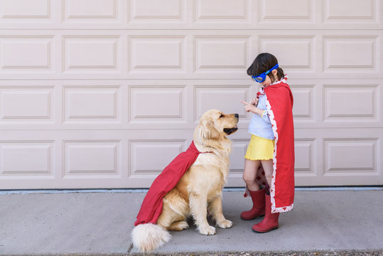 Young girl in super hero cape playing with dog outdoors