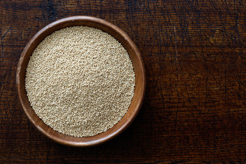 Fototapeta na wymiar Amaranth seeds in dark wooden bowl isolated on dark brown wood from above.