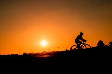 A man rides a bicycle in the evening with orange sky,Silhouette  sporty image concept.