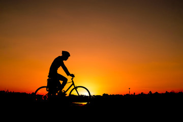 A man rides a bicycle in the evening with orange sky,Silhouette  sporty image concept.