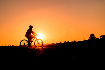 Fototapeta na wymiar A man rides a bicycle in the evening with orange sky,Silhouette sporty image concept.