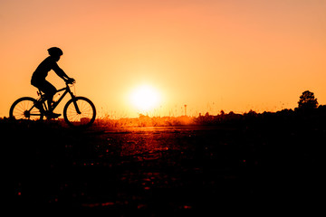 Fototapeta na wymiar A man rides a bicycle in the evening with orange sky,Silhouette sporty image concept.
