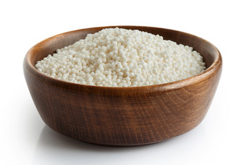 Dry tapioca pearls in dark wooden bowl isolated on white.