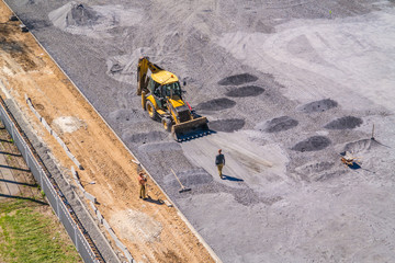 Excavator at the construction site of the school stadium. Heaps of crushed rock