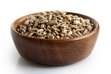 Peeled dry sunflower seeds in dark wooden bowl isolated on white.