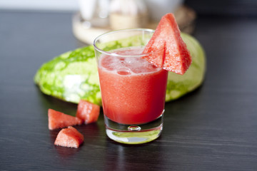 Melonensaft schräg von oben mit dunklem Untergrund und Melonenstücken