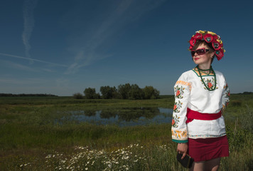 Fototapeta na wymiar National clothes - a girl in Ukrainian embroidery with a wreath on her head by the lake in a meadow among the flowers