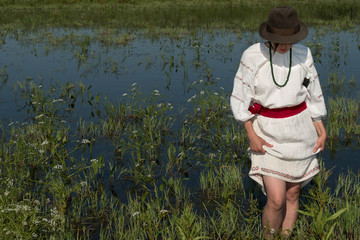 National clothes - a girl standing in a pond in a hat with a machete