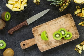 Cutting fresh kiwi and pineapple on wooden board. Top view