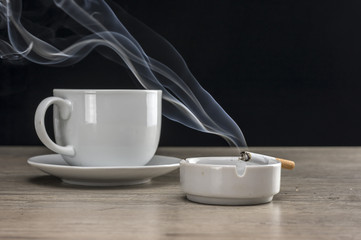 Cup of coffee and lit cigarette burning in ashtray