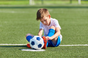 Boy football soccer tying laces him boots on grass