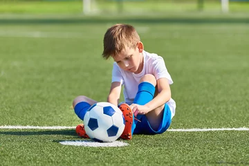 Foto op Plexiglas Boy football soccer tying laces him boots on grass © Sergey Ryzhov