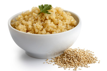 Cooked quinoa in white ceramic bowl isolated on white with green parsley. Spilled uncooked quinoa.