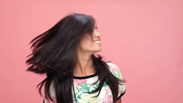 Young smiling asian woman shaking hair over pink background